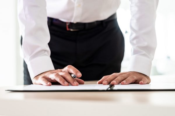 Business employer signing an application form or other important document standing behind his desk.