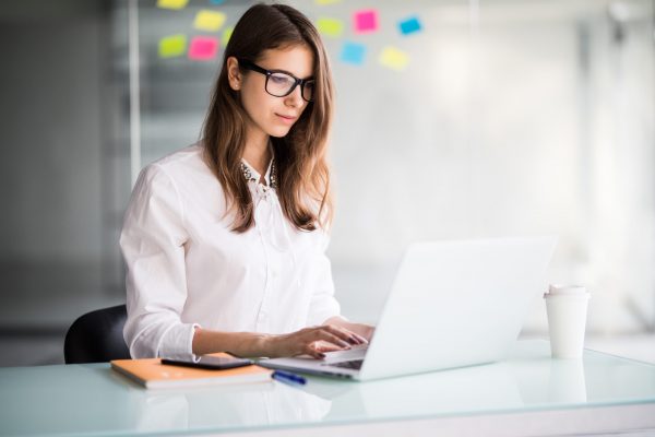 successful businesswoman working on laptop computer in her office dressed up in white strict clothes