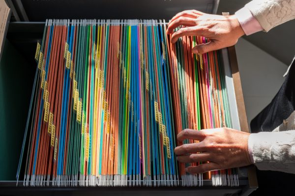 Working women search for colorful files, sorted in filing cabinets.